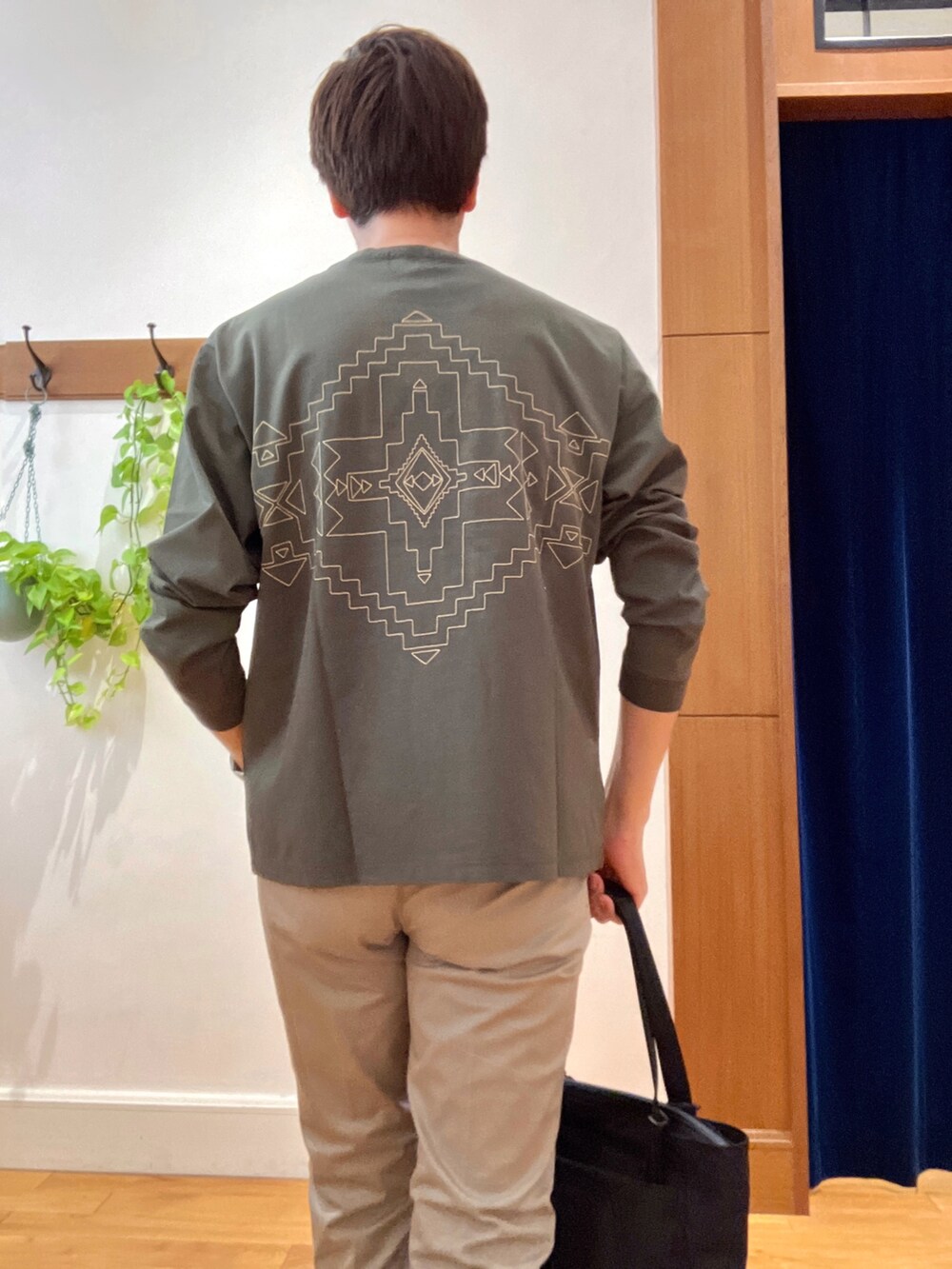 グリーン系のTシャツ/カットソー、グレー系のチノパンツ、ブラック系のトートバッグを着用したメンズの秋コーディネートの2枚目の写真