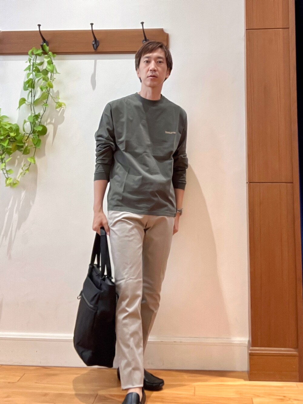 グリーン系のTシャツ/カットソー、グレー系のチノパンツ、ブラック系のトートバッグを着用したメンズの秋コーディネートの8枚目の写真