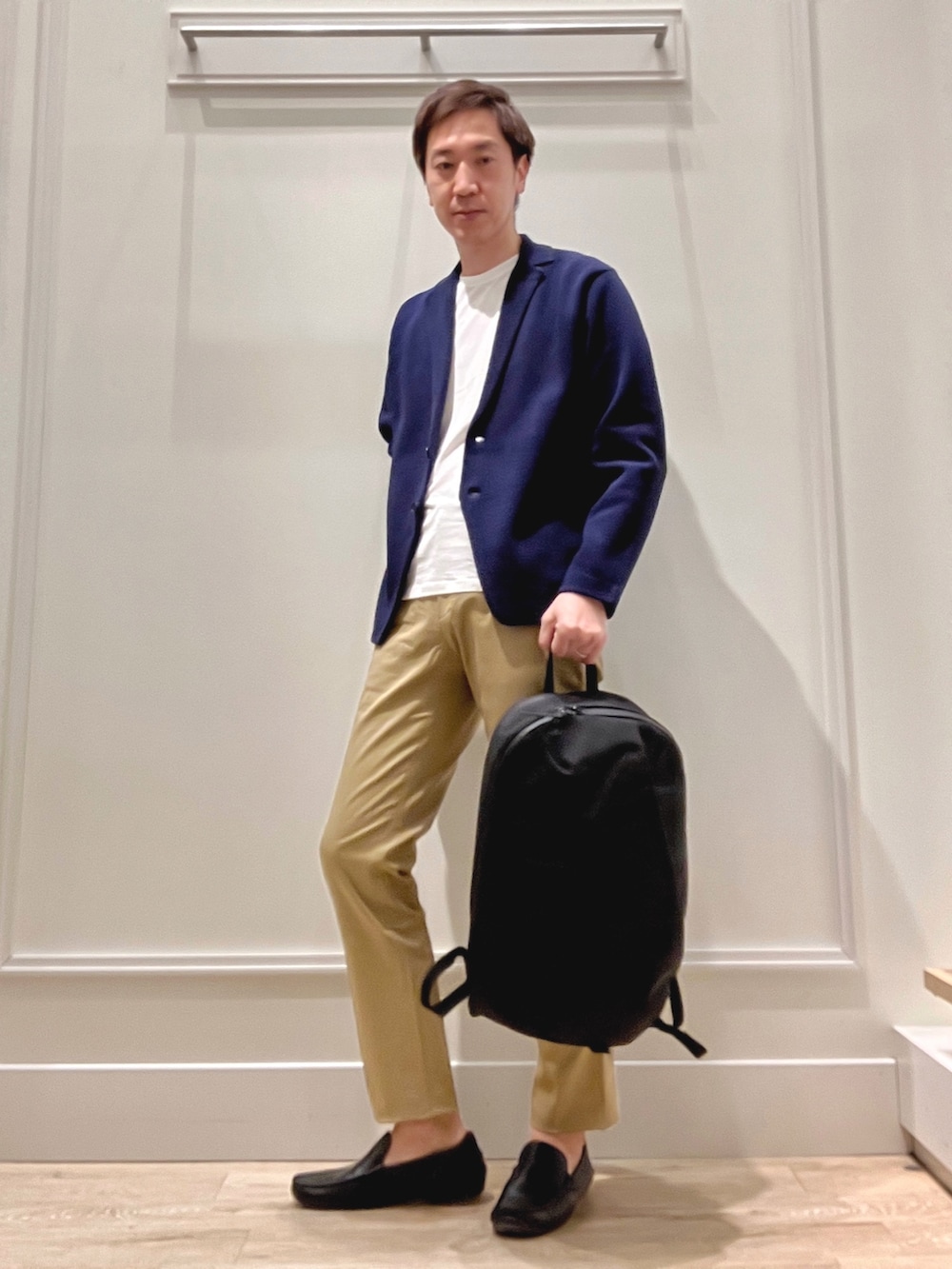 ベージュ系のチノパンツ、ブラック系のバックパック/リュック、ブルー系のカーディガン/ボレロを着用したメンズの冬コーディネートの2枚目の写真