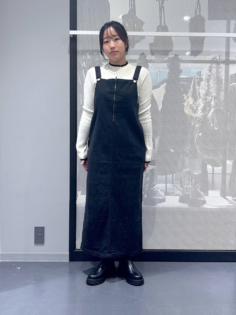 グレー系のジャンパースカート、ブラック系のショルダーバッグ、ブラック系のブーツを着用したレディースの冬コーディネートの4枚目の写真