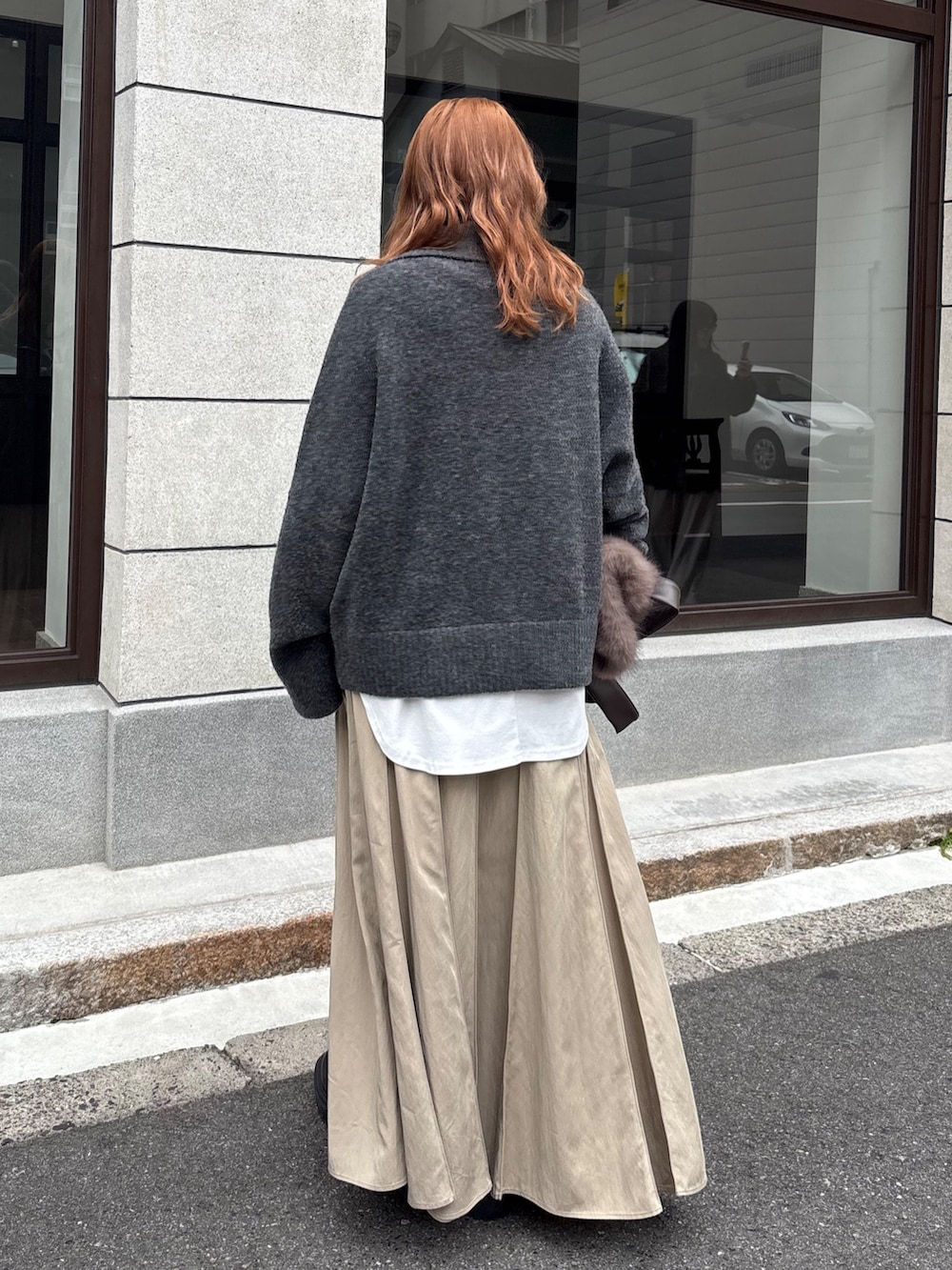 グレー系のカーディガン/ボレロ、ベージュ系のスカート、ブラウン系のショルダーバッグを着用したレディースの秋コーディネートの2枚目の写真