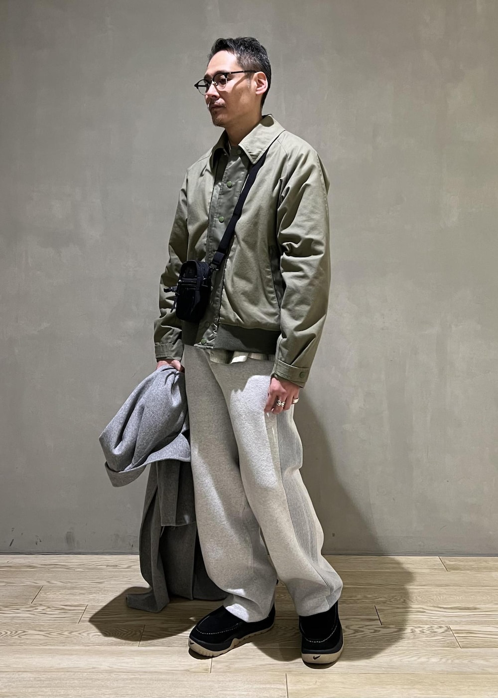 グレー系のステンカラーコート、グレー系のその他パンツ、ブラック系のショルダーバッグを着用したメンズの冬コーディネートの7枚目の写真