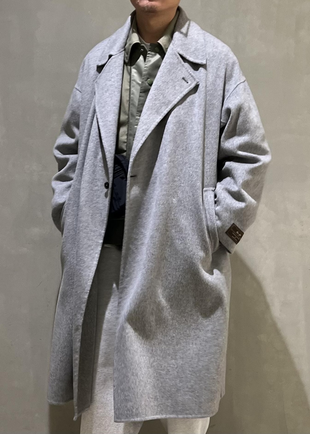 グレー系のステンカラーコート、グレー系のその他パンツ、ブラック系のショルダーバッグを着用したメンズの冬コーディネートの4枚目の写真