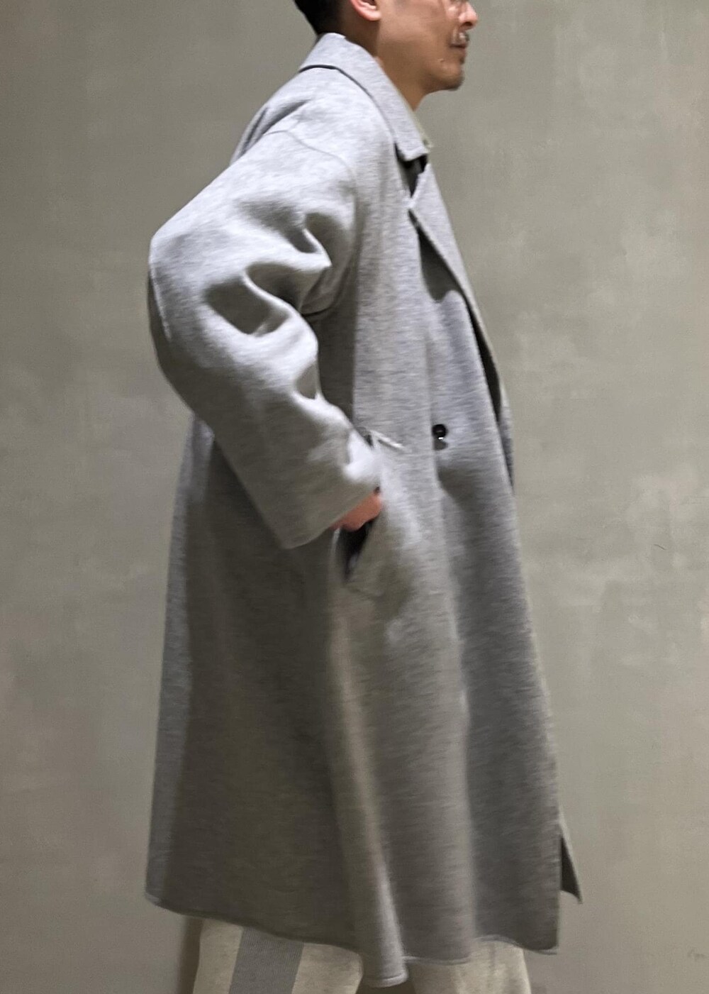 グレー系のステンカラーコート、グレー系のその他パンツ、ブラック系のショルダーバッグを着用したメンズの冬コーディネートの5枚目の写真