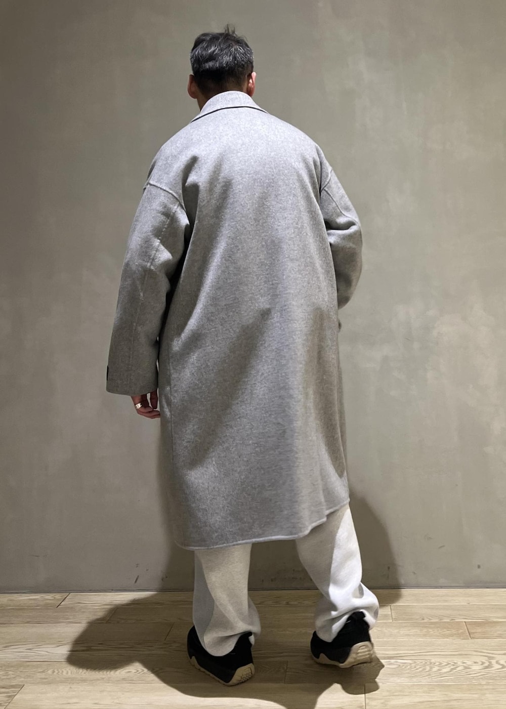 グレー系のステンカラーコート、グレー系のその他パンツ、ブラック系のショルダーバッグを着用したメンズの冬コーディネートの3枚目の写真