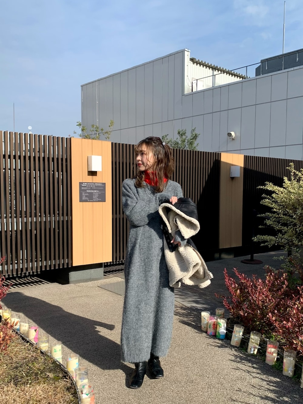 ブラック系のムートンコート、グレー系のワンピース、レッド系のニット/セーターを着用したレディースの冬コーディネートの2枚目の写真