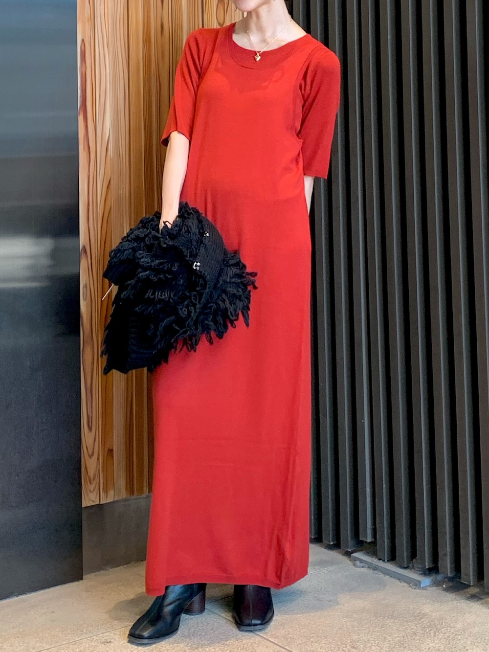 レッド系のワンピース、ブラック系のベスト、ブラック系のブーツを着用したレディースの秋コーディネートの6枚目の写真