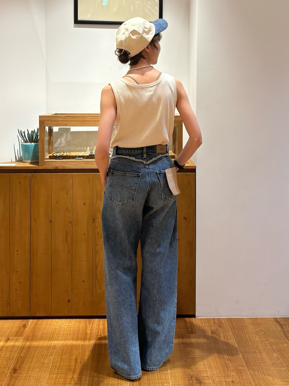 ブルー系のデニムパンツ、ホワイト系のタンクトップ、ホワイト系のキャップを着用したレディースの夏コーディネートの3枚目の写真