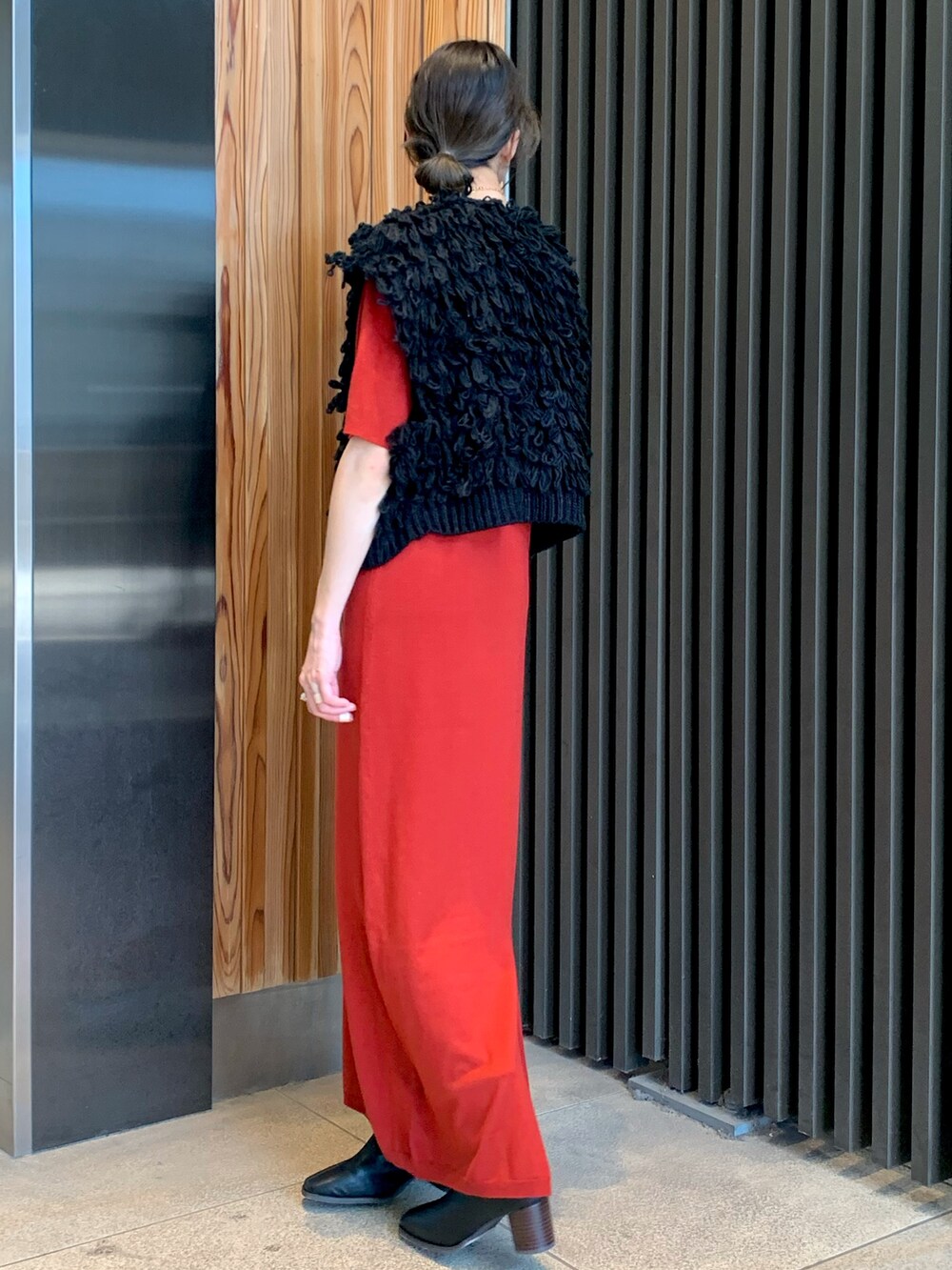 レッド系のワンピース、ブラック系のベスト、ブラック系のブーツを着用したレディースの秋コーディネートの3枚目の写真