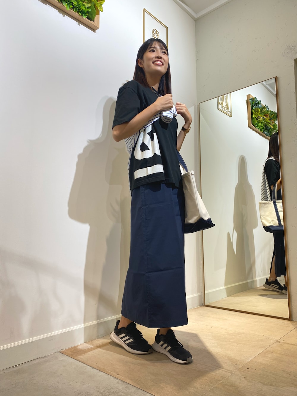 ブラック系のTシャツ/カットソー、ブルー系のトートバッグ、ブルー系のスカートを着用したレディースの秋コーディネートの2枚目の写真