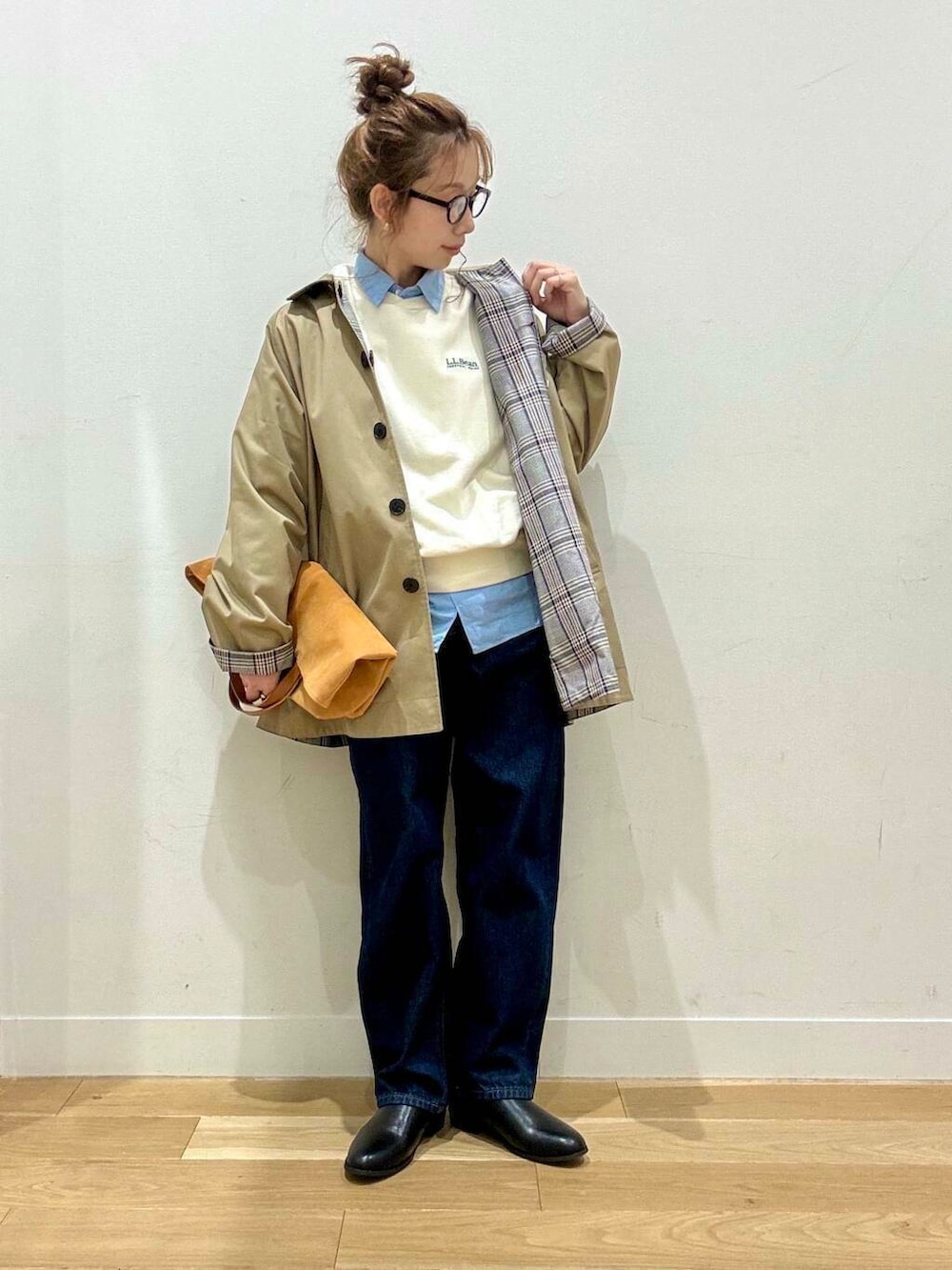 ベージュ系のステンカラーコート、イエロー系のトートバッグ、ブルー系のデニムパンツを着用したレディースの秋コーディネートの2枚目の写真