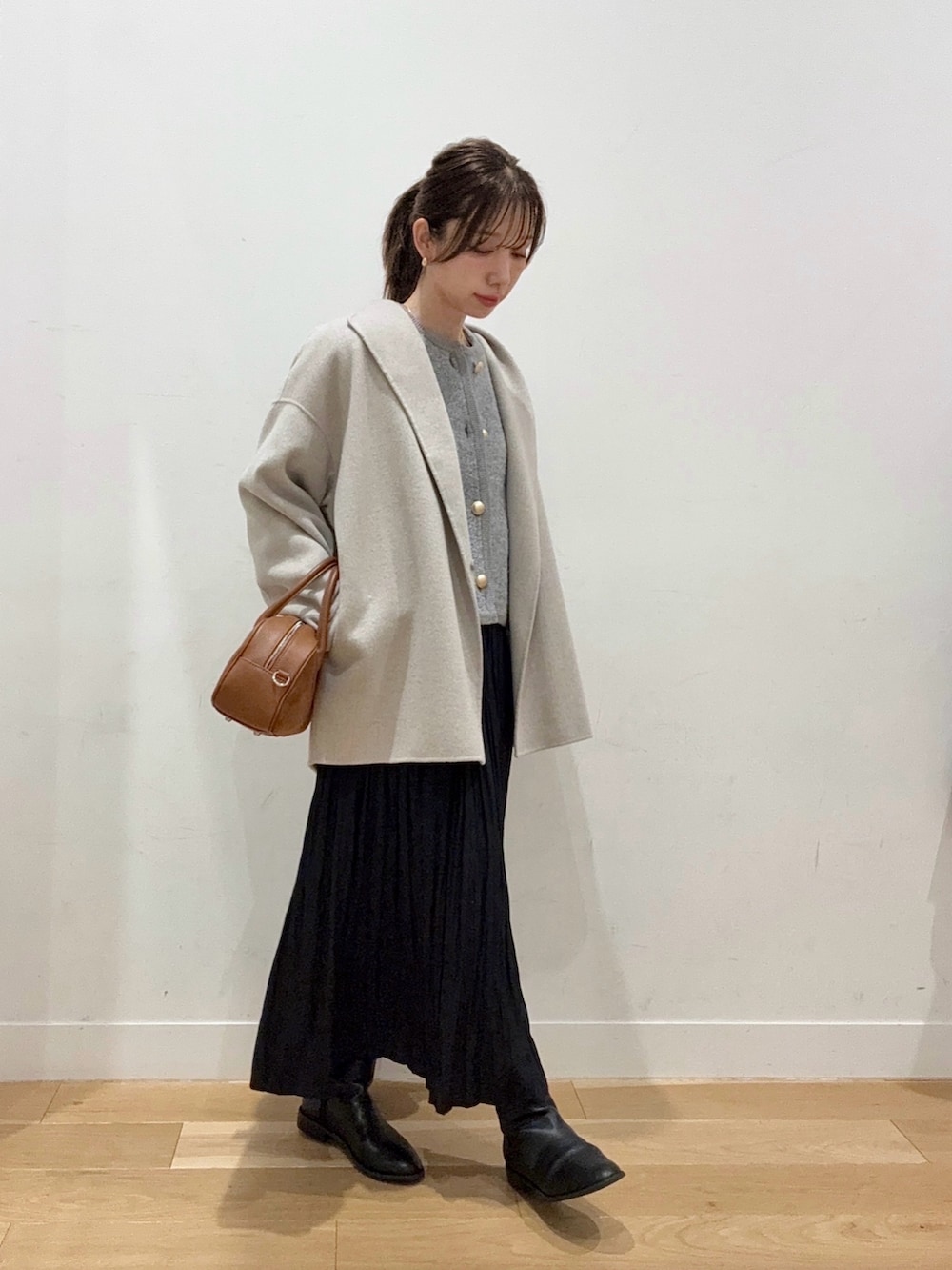ブラウン系のショルダーバッグ、ブラック系のブーツ、ブラック系のスカートを着用したレディースの秋コーディネートの2枚目の写真
