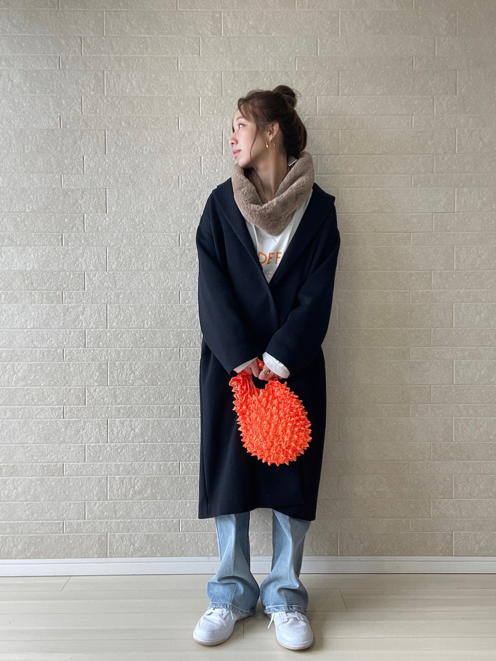 ブルー系のチェスターコート、ブルー系のデニムパンツ、オレンジ系のエコバッグ/サブバッグを着用したレディースの秋コーディネートの2枚目の写真