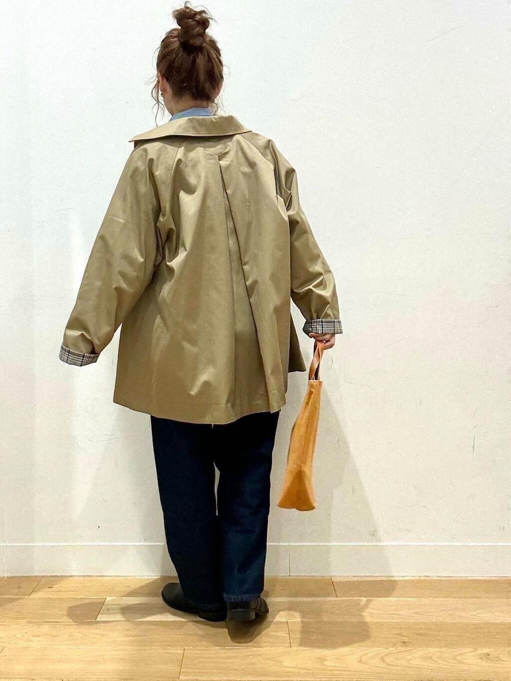 ベージュ系のステンカラーコート、イエロー系のトートバッグ、ブルー系のデニムパンツを着用したレディースの秋コーディネートの3枚目の写真