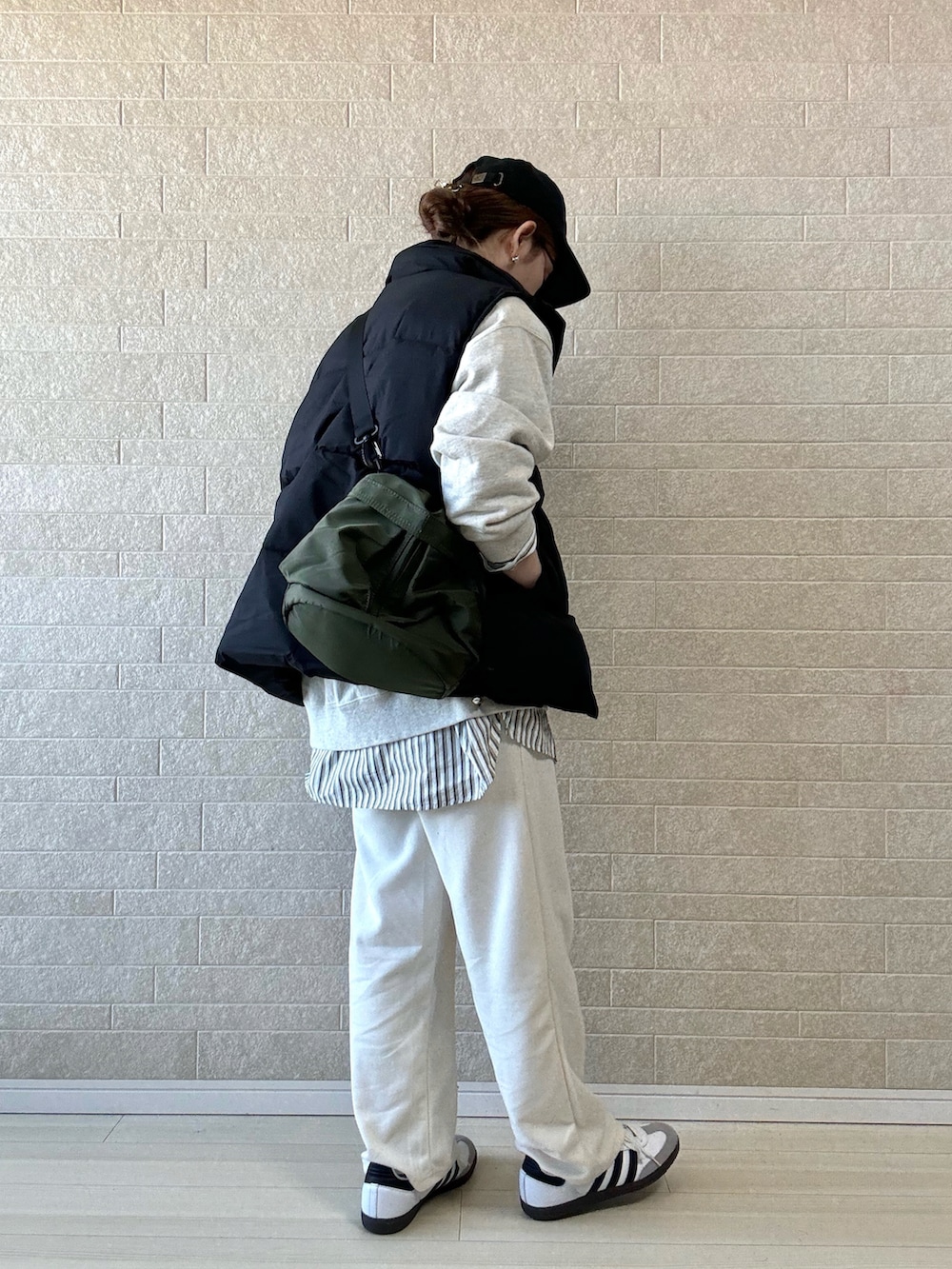 ブラック系のダウンベスト、ホワイト系のスウェットパンツ、グリーン系のショルダーバッグを着用したレディースの秋コーディネートの2枚目の写真