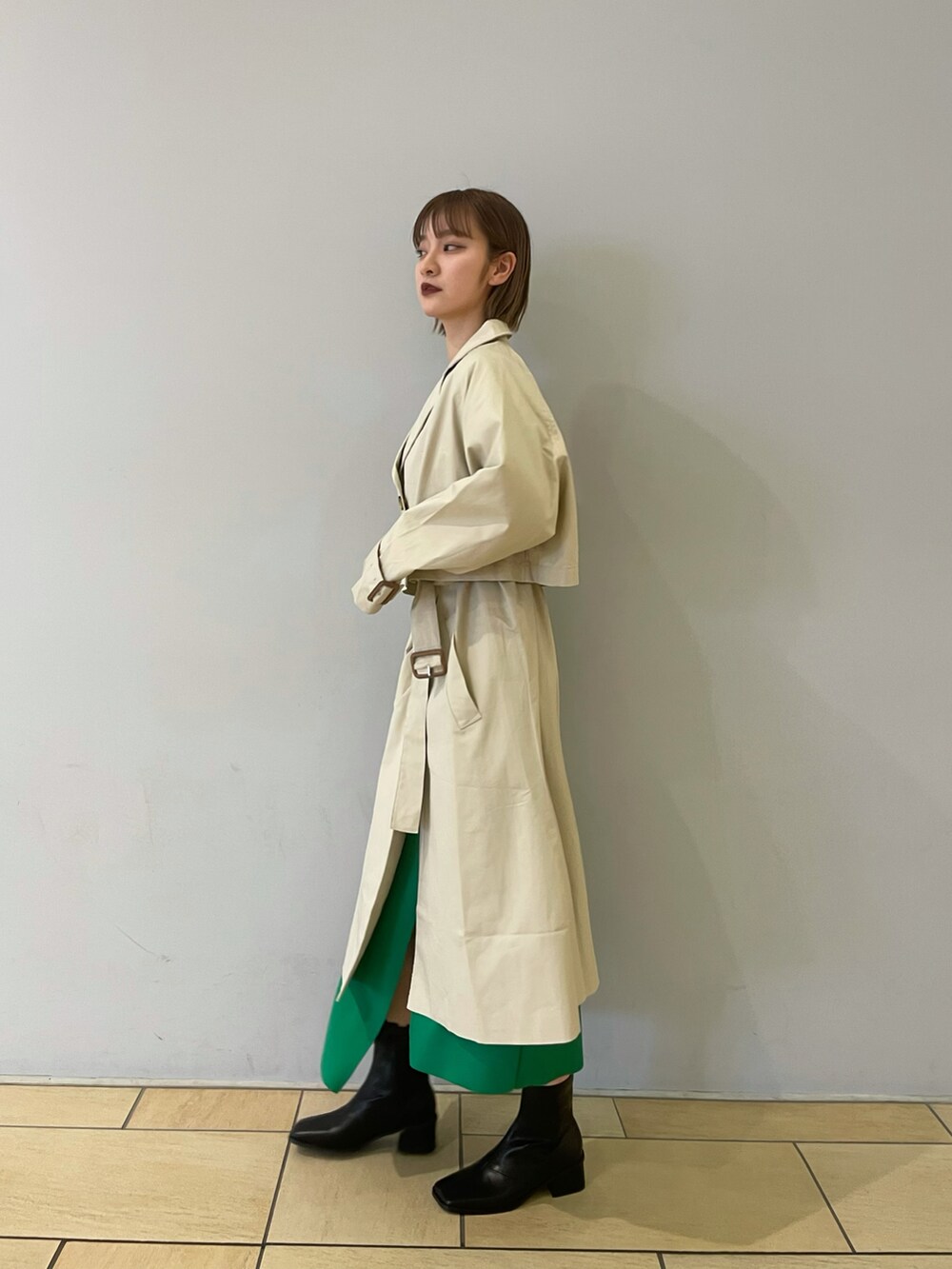 ベージュ系のトレンチコート、グリーン系のスカート、ブラック系のブーツを着用したレディースの冬コーディネートの4枚目の写真