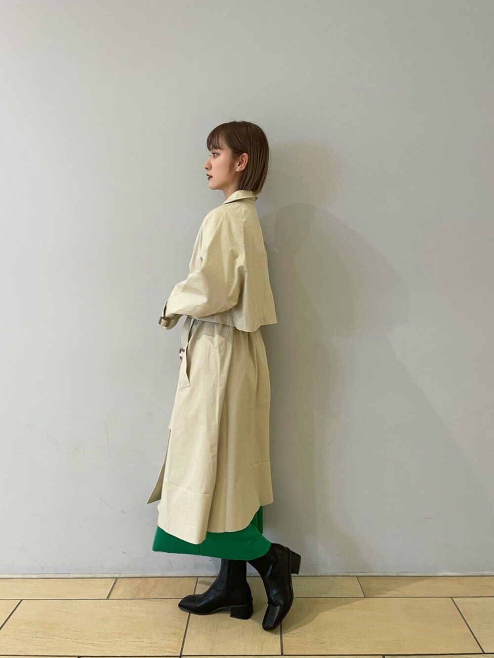 ベージュ系のトレンチコート、グリーン系のスカート、ブラック系のブーツを着用したレディースの冬コーディネートの2枚目の写真