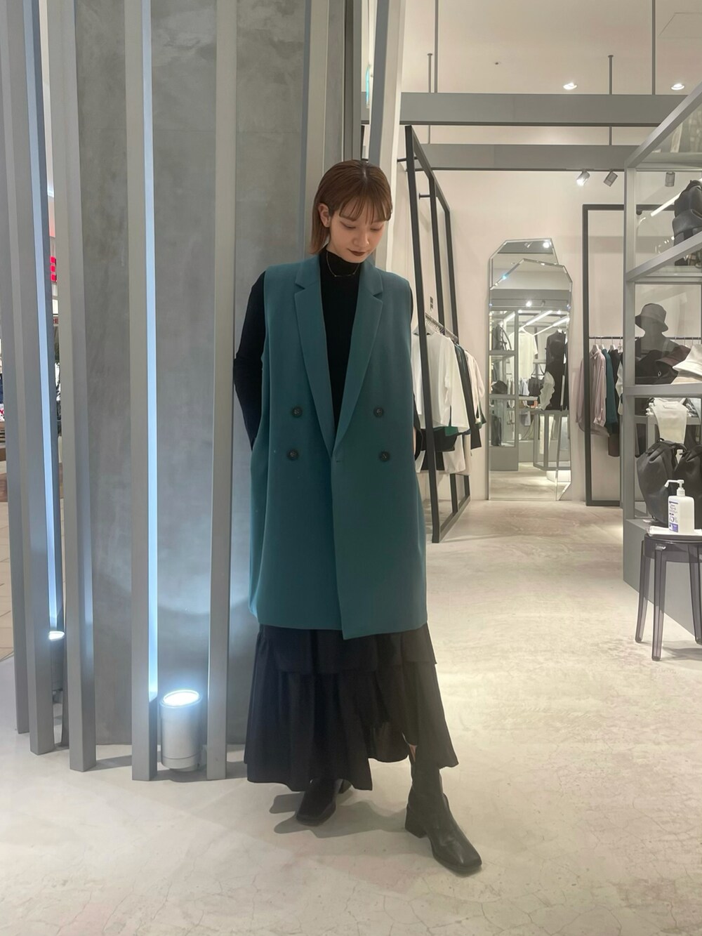 ブラック系のスカート、ブラック系のブーツ、グリーン系のベストを着用したレディースの春コーディネートの2枚目の写真