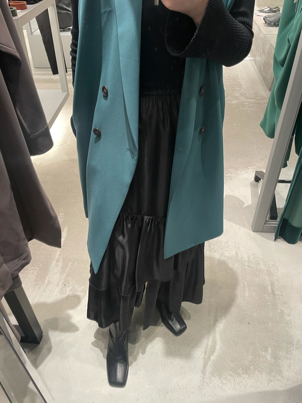 ブラック系のスカート、ブラック系のブーツ、グリーン系のベストを着用したレディースの春コーディネートの4枚目の写真