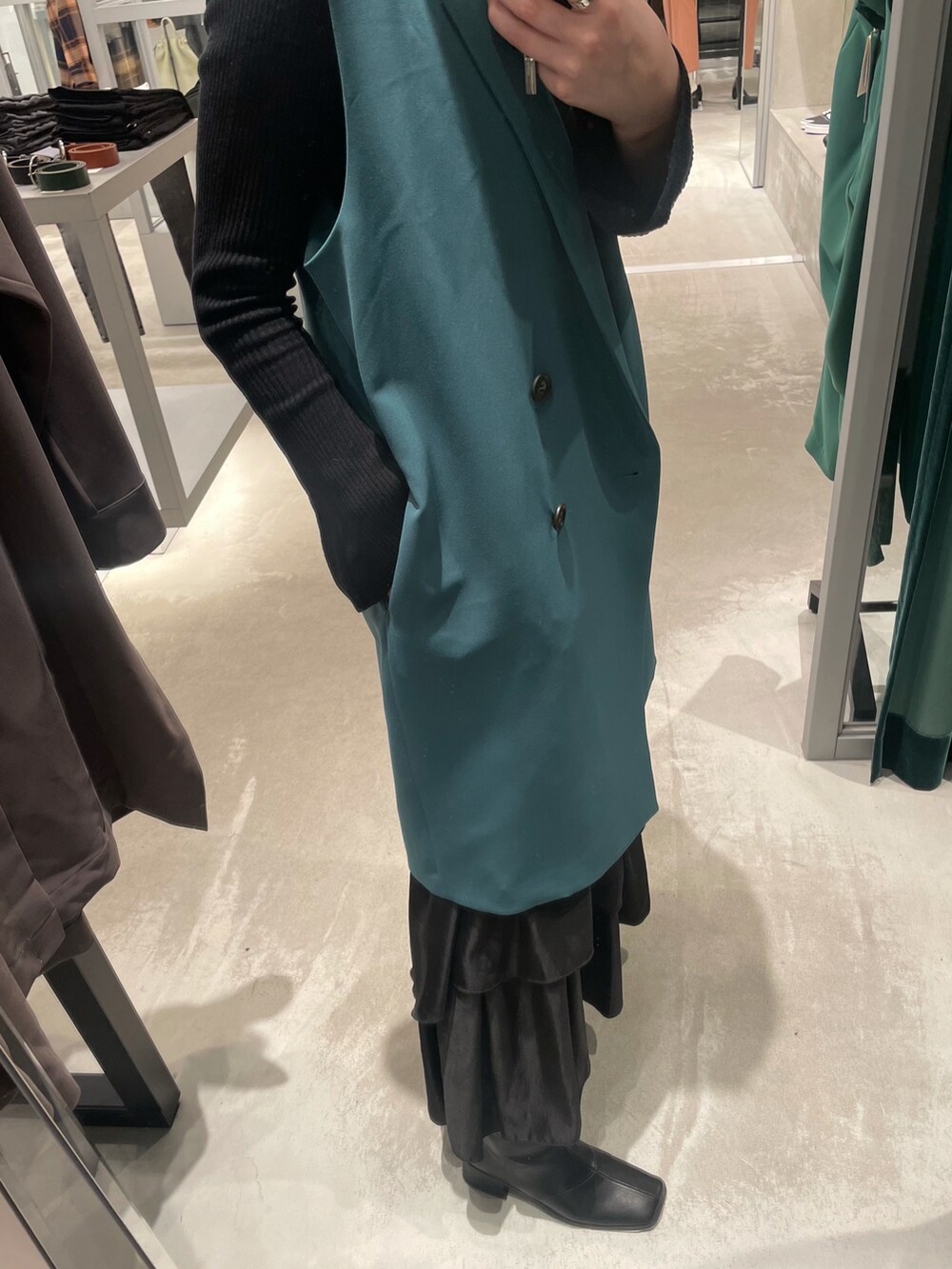 ブラック系のスカート、ブラック系のブーツ、グリーン系のベストを着用したレディースの春コーディネートの3枚目の写真