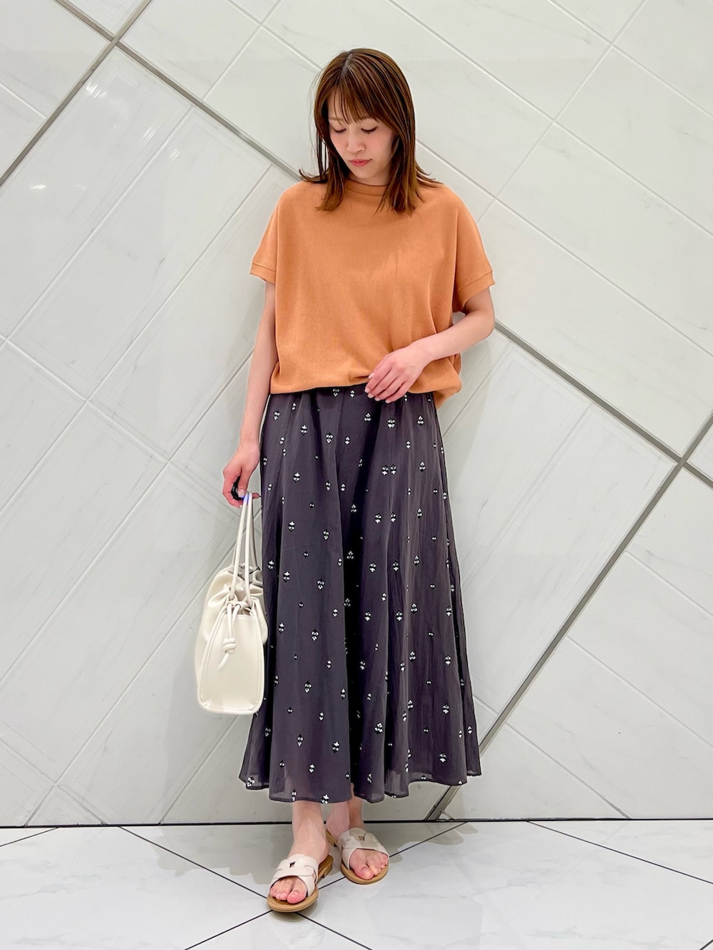 レッド系のTシャツ/カットソー、グレー系のスカート、ホワイト系のトートバッグを着用したレディースの春コーディネートの3枚目の写真