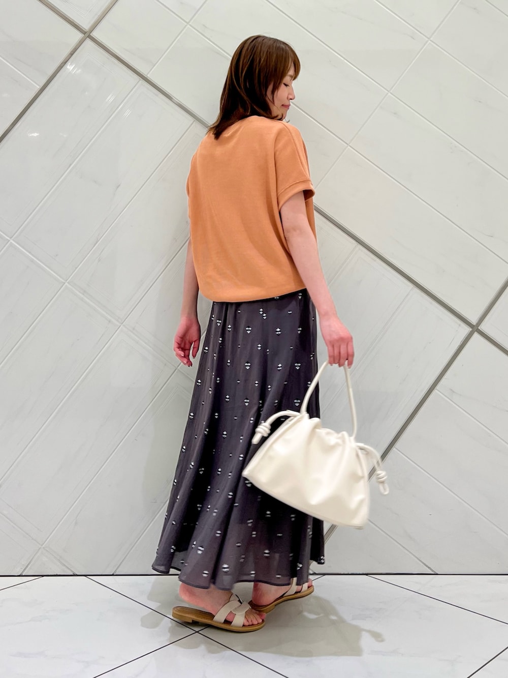レッド系のTシャツ/カットソー、グレー系のスカート、ホワイト系のトートバッグを着用したレディースの春コーディネートの2枚目の写真