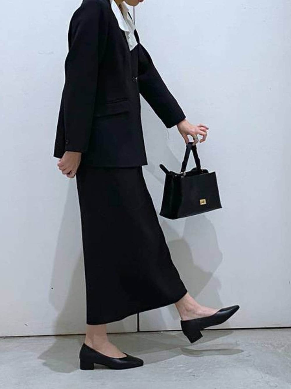 ブラック系のパンプス、ブラック系のスカート、ブラック系のショルダーバッグを着用したレディースの冬コーディネートの4枚目の写真