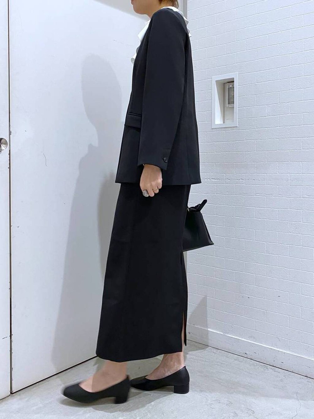 ブラック系のパンプス、ブラック系のスカート、ブラック系のショルダーバッグを着用したレディースの冬コーディネートの2枚目の写真