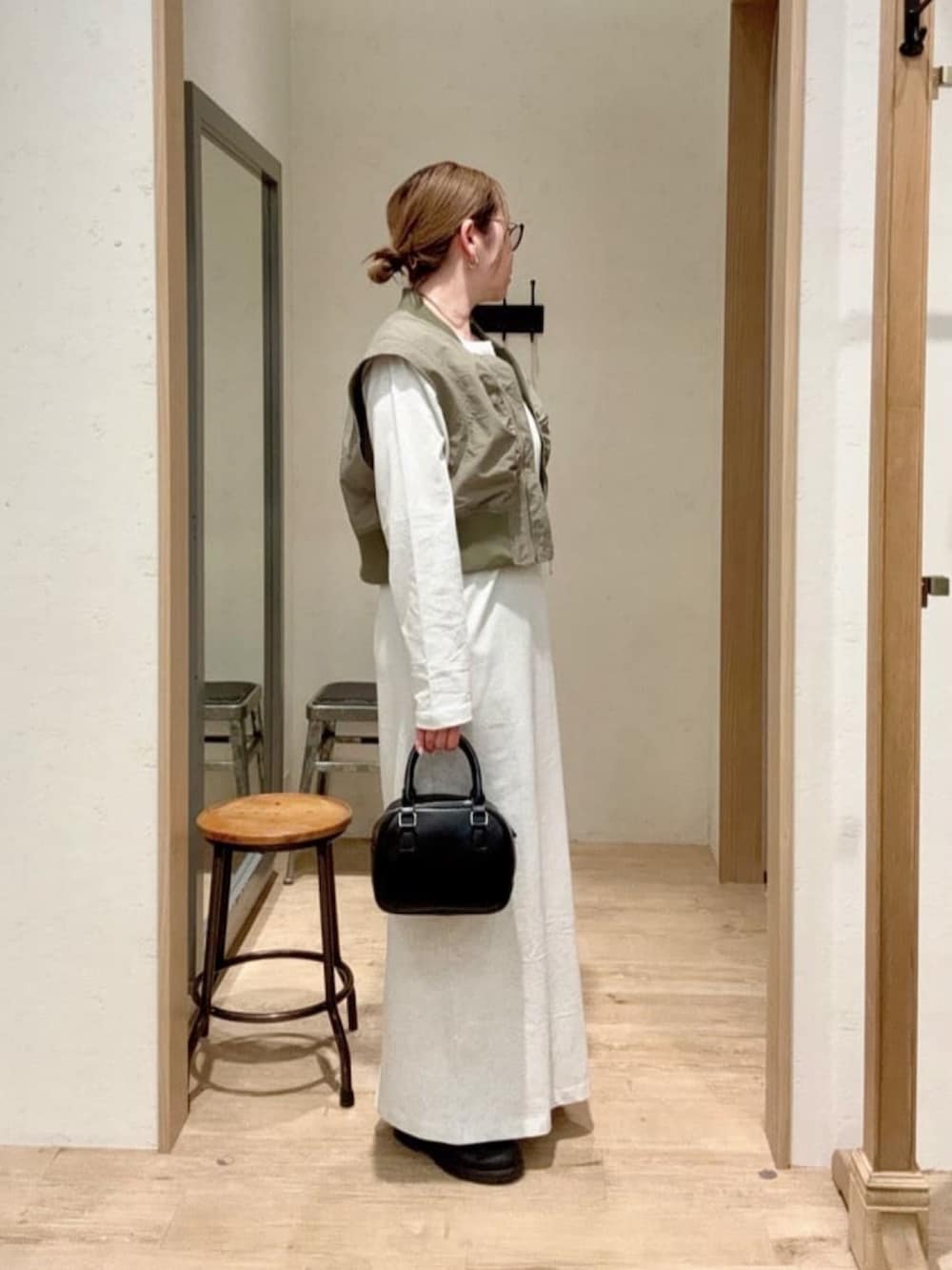 グリーン系のベスト、グレー系のワンピース、ブラック系のショルダーバッグを着用したレディースの春コーディネートの2枚目の写真
