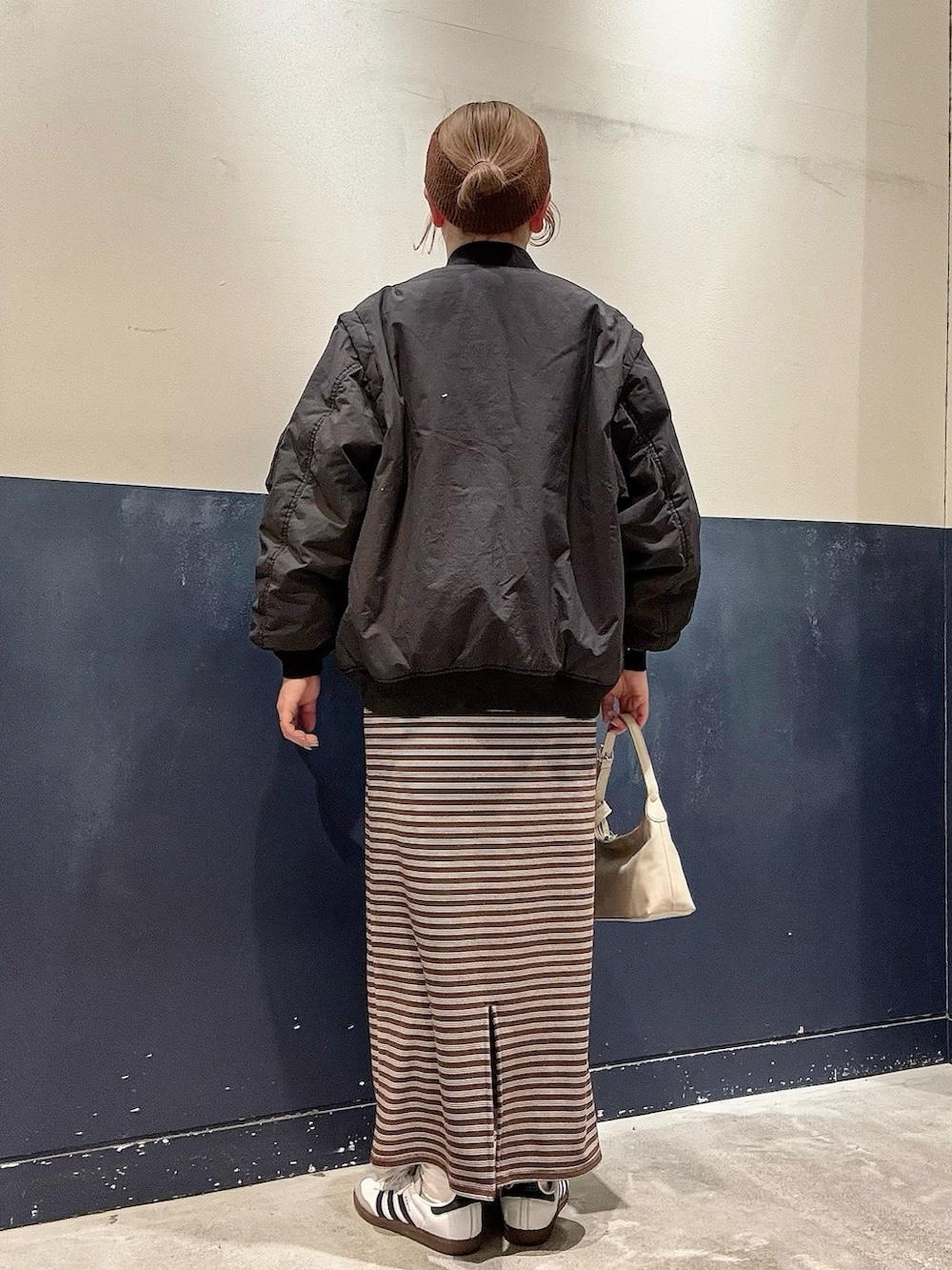 グレー系のショルダーバッグ、ブラウン系のワンピース、ブラック系のMA-1を着用したレディースの冬コーディネートの3枚目の写真