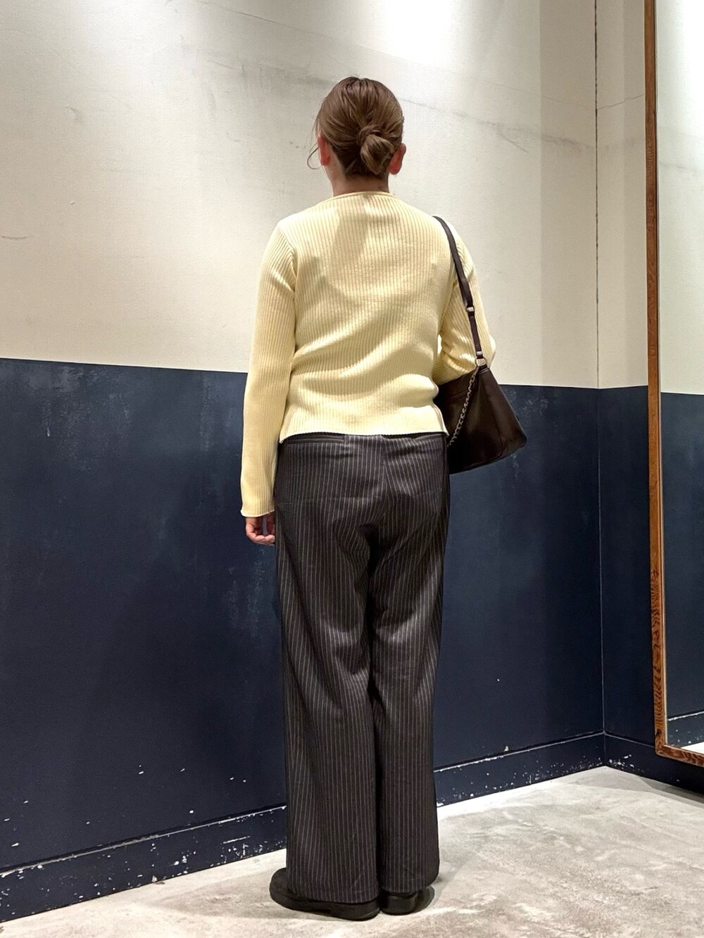 グレー系のスラックス、ブラウン系のショルダーバッグ、イエロー系のカーディガン/ボレロを着用したレディースの冬コーディネートの3枚目の写真