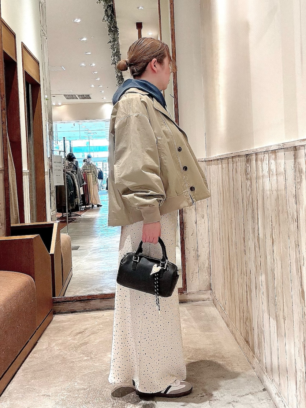 ブラック系のショルダーバッグ、ホワイト系のスカート、ベージュ系のトレンチコートを着用したレディースの春コーディネートの2枚目の写真