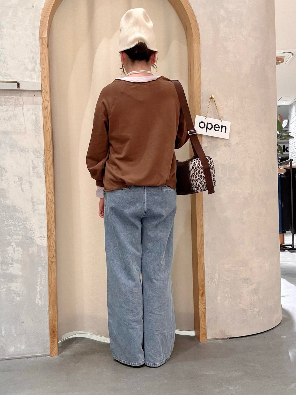 ブラウン系のスウェット、ブラウン系のトートバッグ、ブルー系のデニムパンツを着用したレディースの秋コーディネートの3枚目の写真