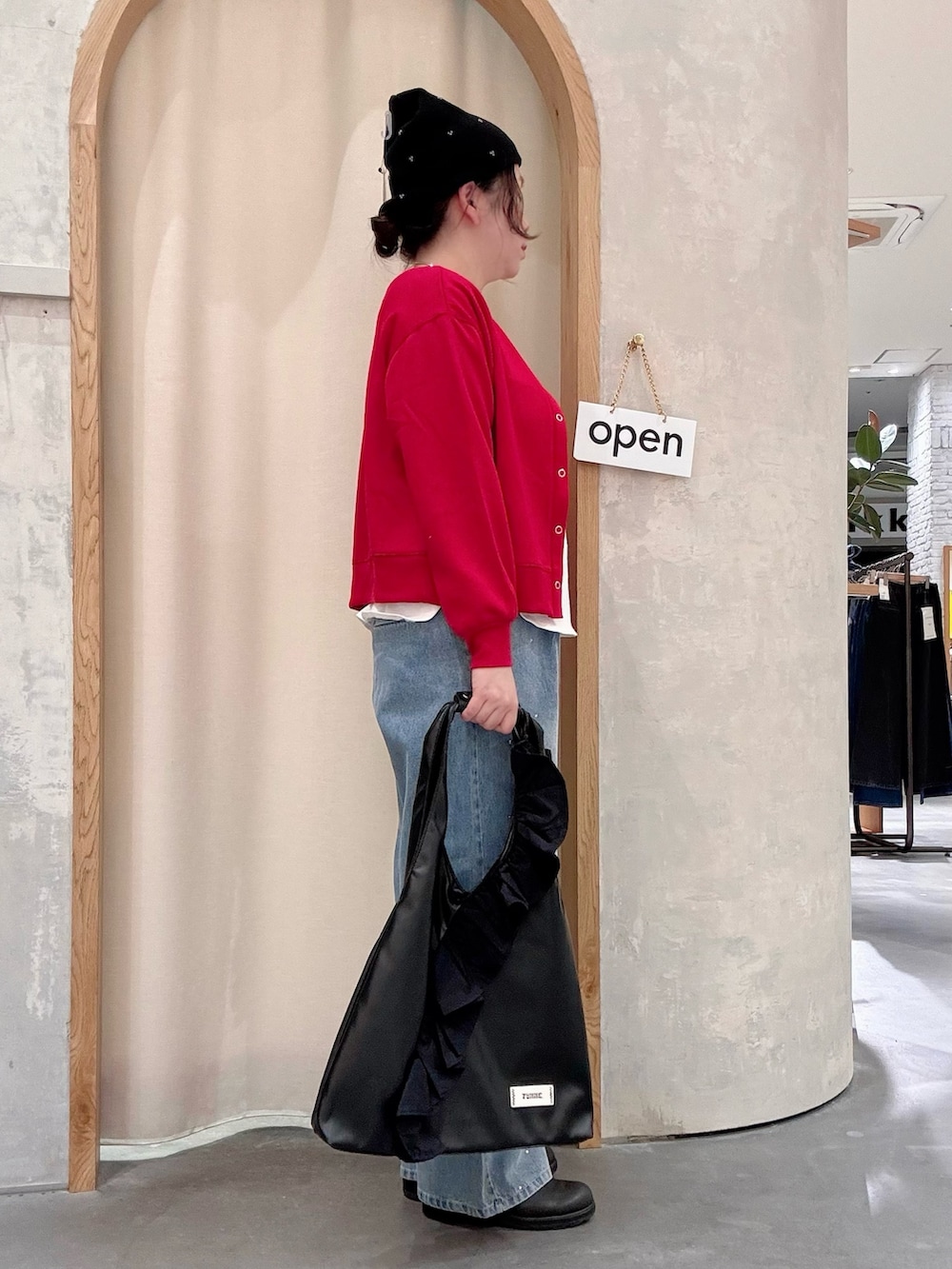 ブラック系のトートバッグ、ブルー系のデニムパンツ、レッド系のカーディガン/ボレロを着用したレディースの秋コーディネートの2枚目の写真
