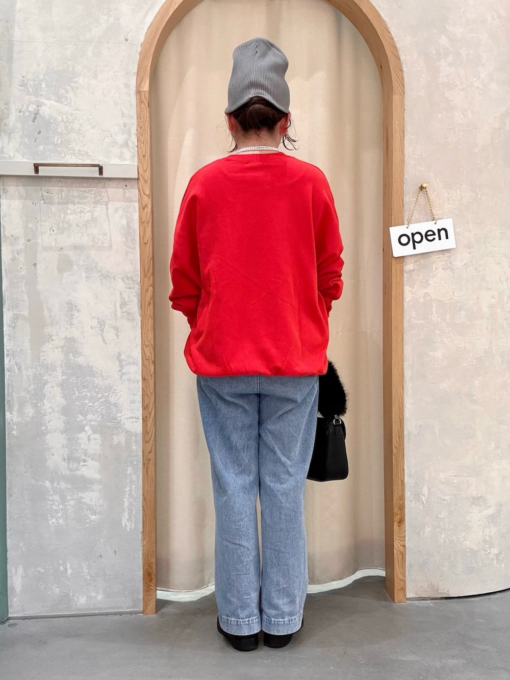 ブラック系のショルダーバッグ、ブルー系のデニムパンツ、レッド系のスウェットを着用したレディースの秋コーディネートの3枚目の写真