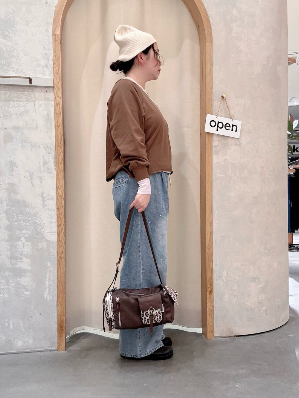 ブラウン系のスウェット、ブラウン系のトートバッグ、ブルー系のデニムパンツを着用したレディースの秋コーディネートの2枚目の写真