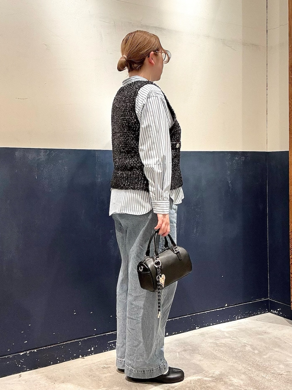 ブルー系のデニムパンツ、ブラック系のショルダーバッグ、ブラック系のベストを着用したレディースの冬コーディネートの2枚目の写真