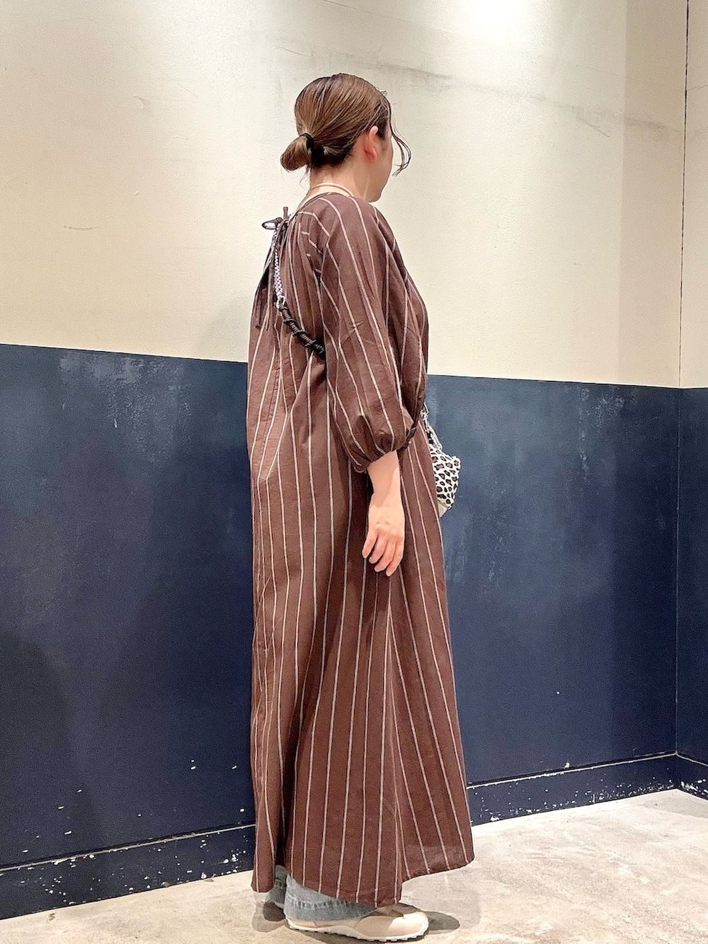 ホワイト系のスニーカー、ブルー系のデニムパンツ、ブラウン系のワンピースを着用したレディースの春コーディネートの2枚目の写真