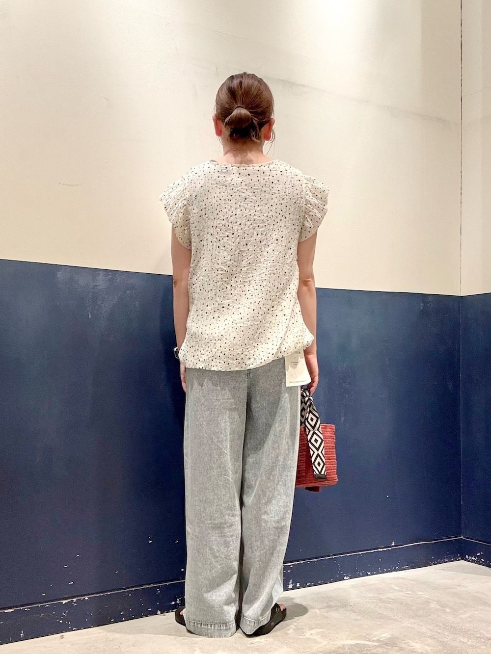レッド系のトートバッグ、ブルー系のデニムパンツ、ホワイト系のシャツ/ブラウスを着用したレディースの夏コーディネートの3枚目の写真