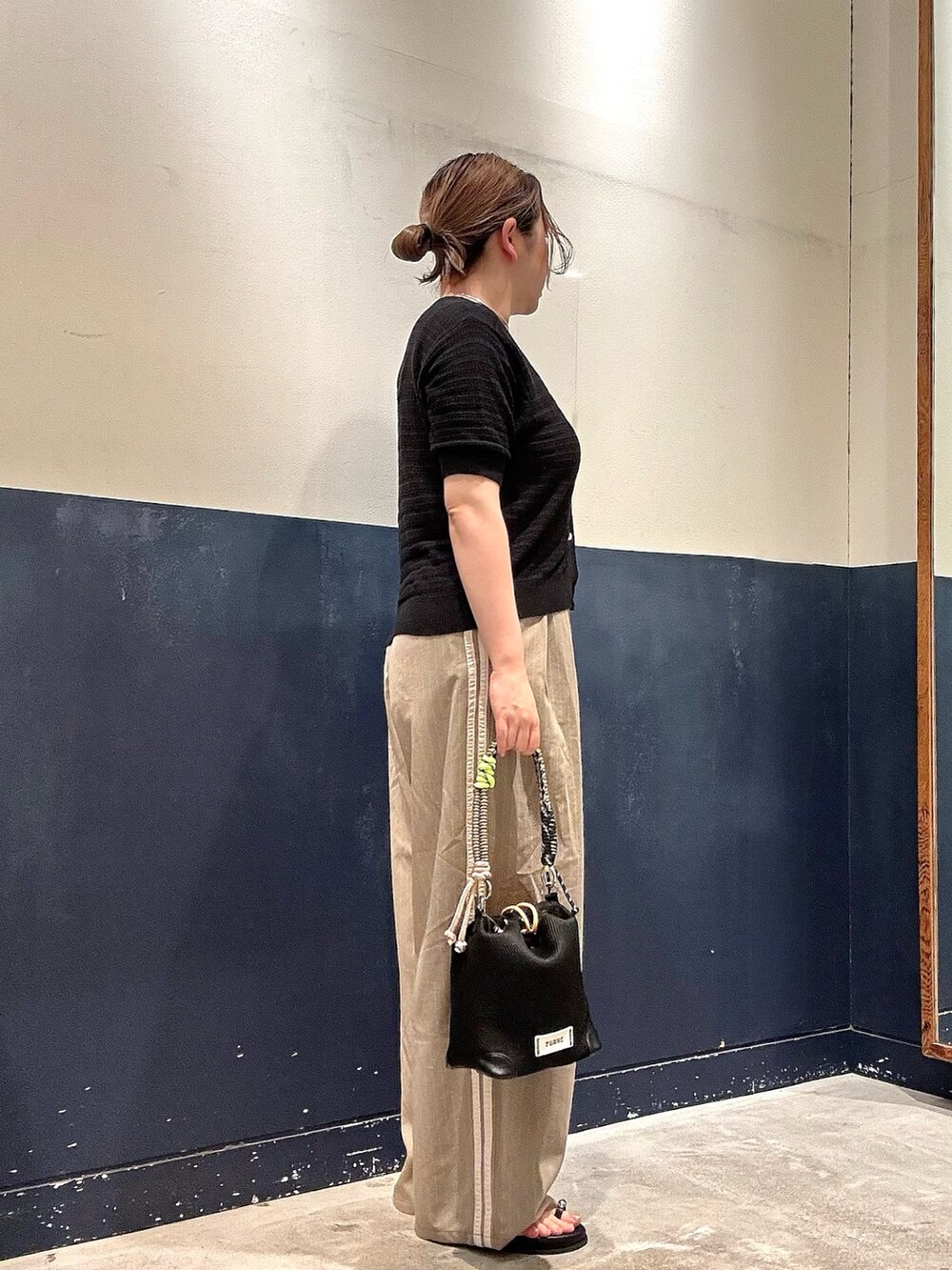ベージュ系のスラックス、ブラック系のショルダーバッグ、ブラック系のTシャツ/カットソーを着用したレディースの夏コーディネートの2枚目の写真