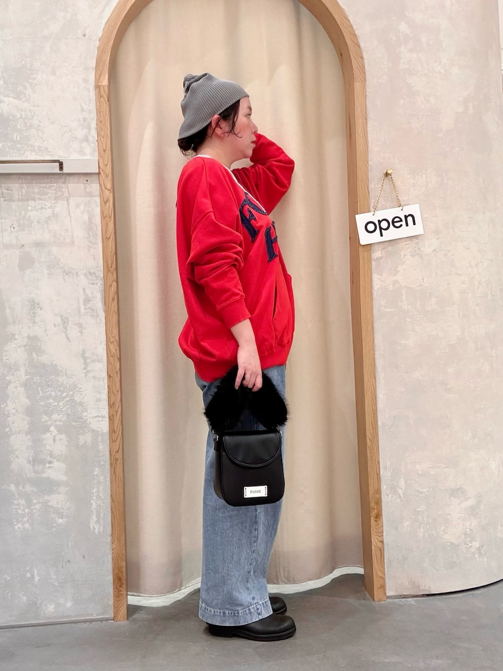 ブラック系のショルダーバッグ、ブルー系のデニムパンツ、レッド系のスウェットを着用したレディースの秋コーディネートの2枚目の写真