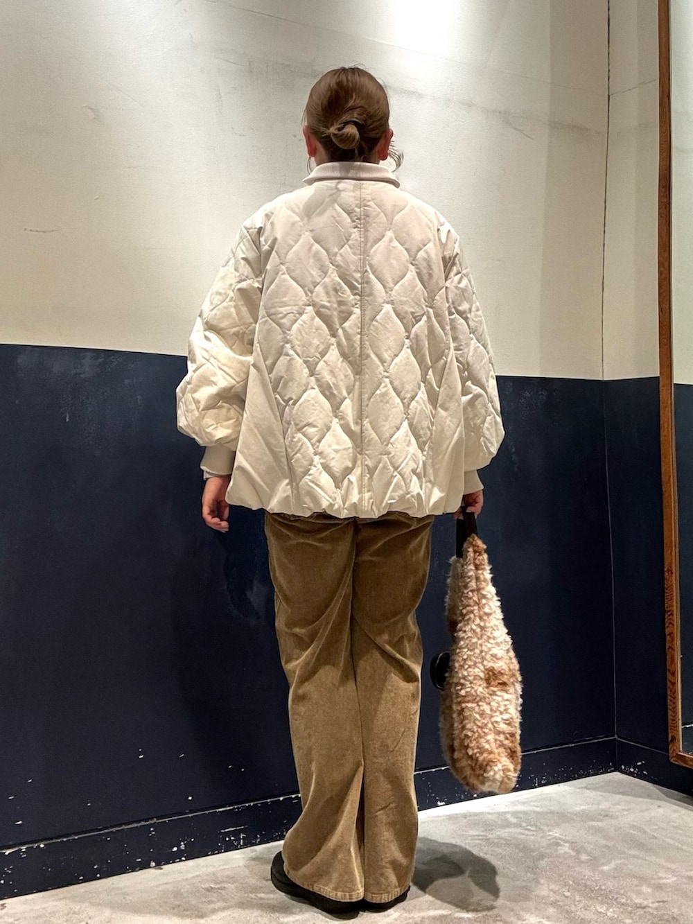 イエロー系のデニムパンツ、ホワイト系のブルゾン、ベージュ系のトートバッグを着用したレディースの冬コーディネートの3枚目の写真