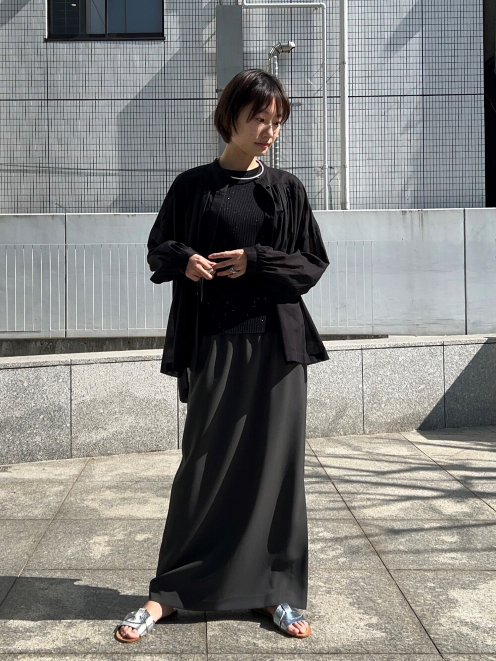 ブラック系のニット/セーター、グレー系のスカート、ブラック系のシャツ/ブラウスを着用したレディースの春コーディネートの2枚目の写真