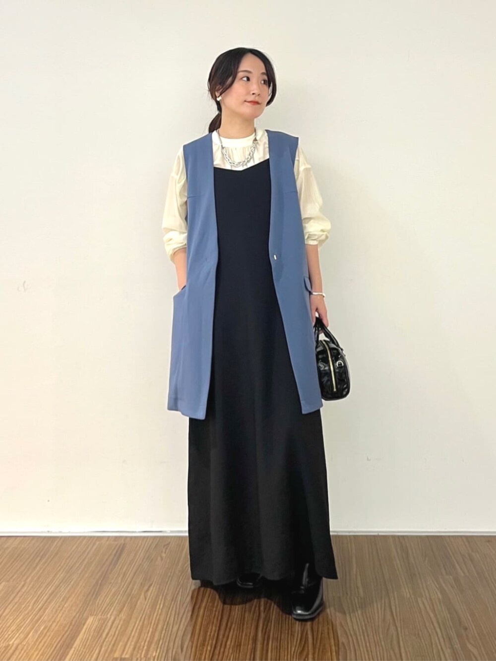 ブラック系のワンピース、ブルー系のベスト、ホワイト系のシャツ/ブラウスを着用したレディースの秋コーディネートの2枚目の写真