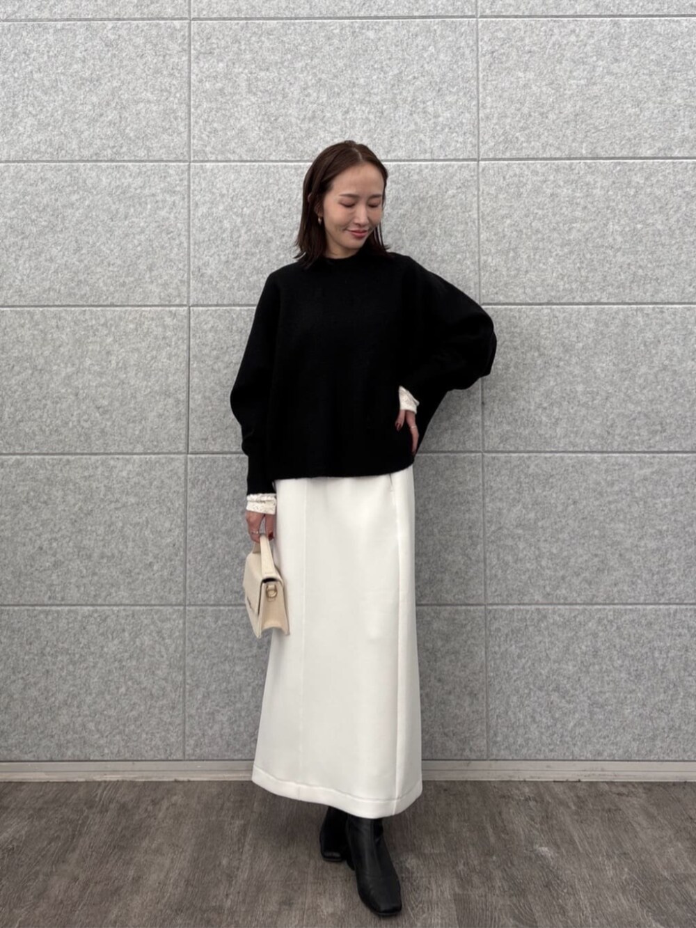 ホワイト系のスカート、ホワイト系のTシャツ/カットソー、ブラック系のニット/セーターを着用したレディースの秋コーディネートの2枚目の写真