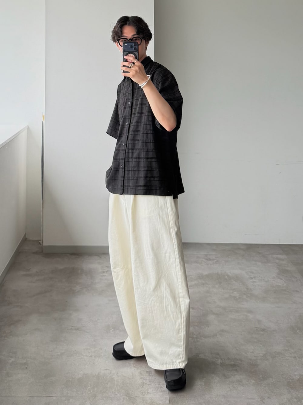 ブラック系のシャツ/ブラウス、ホワイト系のスラックス、ブラック系のモカシン/デッキシューズを着用したメンズの夏コーディネートの2枚目の写真