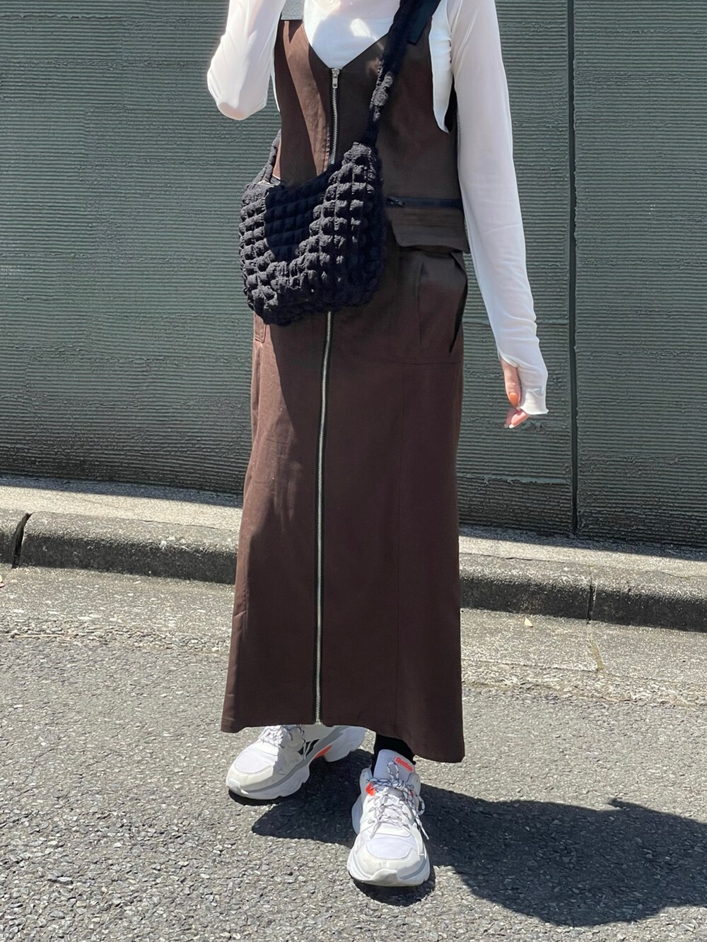 ブラウン系のジャンパースカート、ホワイト系のスニーカー、ブラック系のショルダーバッグを着用したレディースの春コーディネートの4枚目の写真