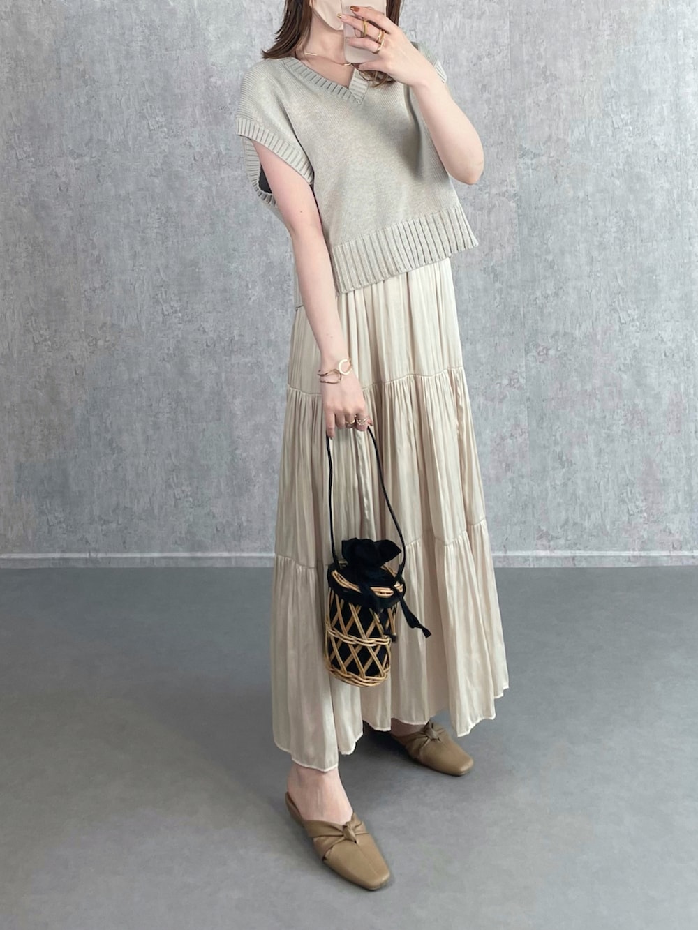 グレー系のベスト、ホワイト系のスカート、ブラック系のかごバッグを着用したレディースの秋コーディネートの3枚目の写真