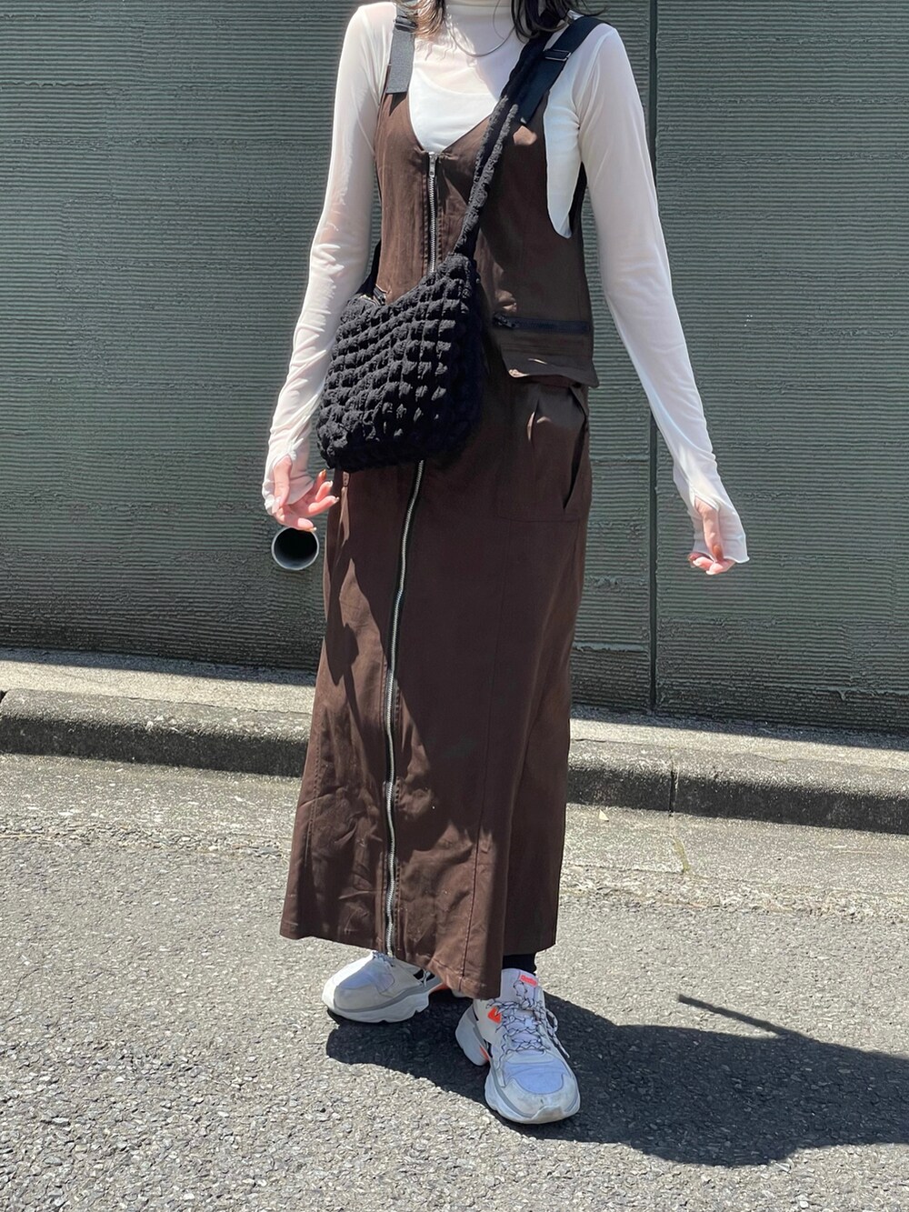 ブラウン系のジャンパースカート、ホワイト系のスニーカー、ブラック系のショルダーバッグを着用したレディースの春コーディネートの2枚目の写真