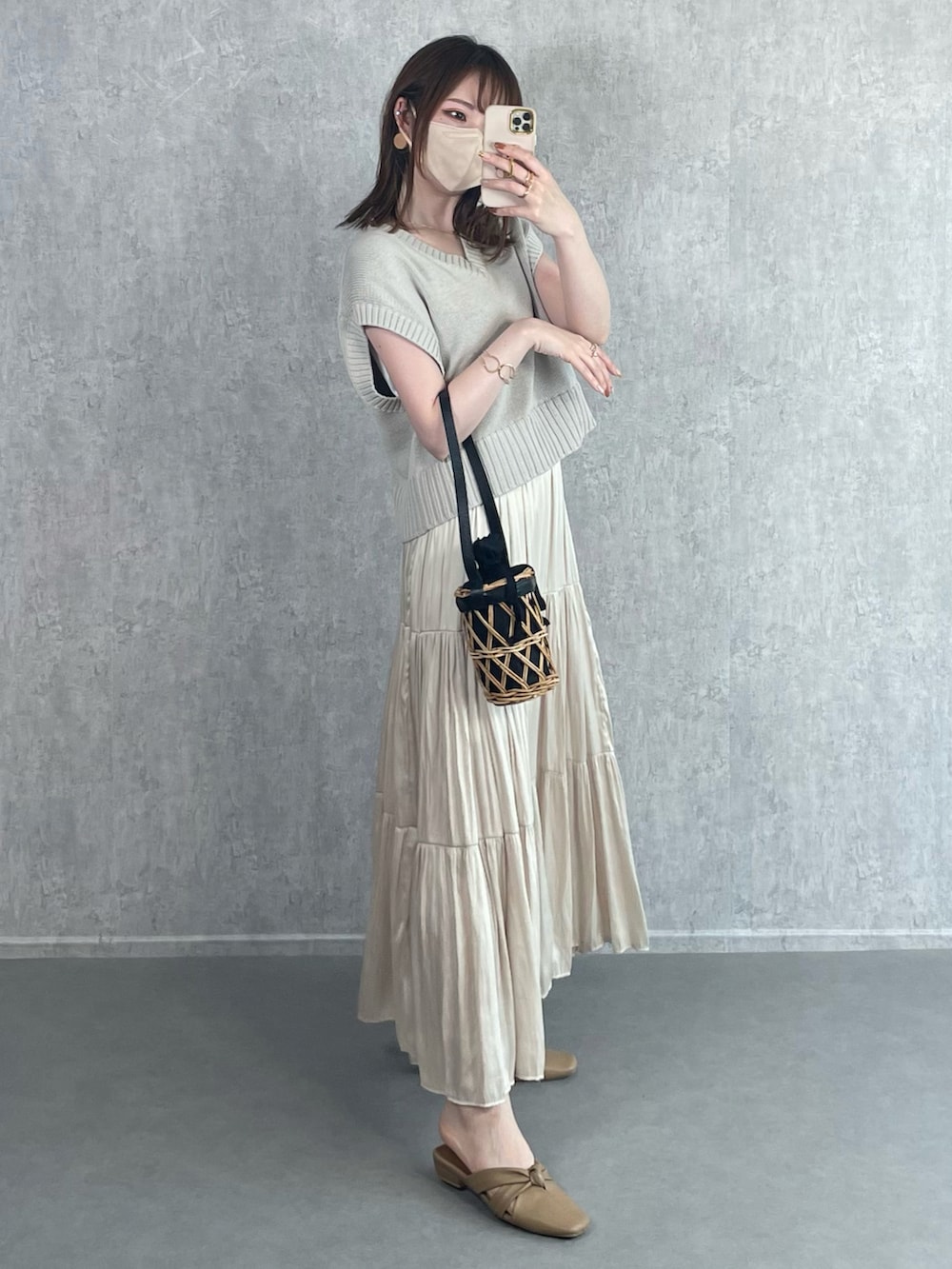 グレー系のベスト、ホワイト系のスカート、ブラック系のかごバッグを着用したレディースの秋コーディネートの4枚目の写真